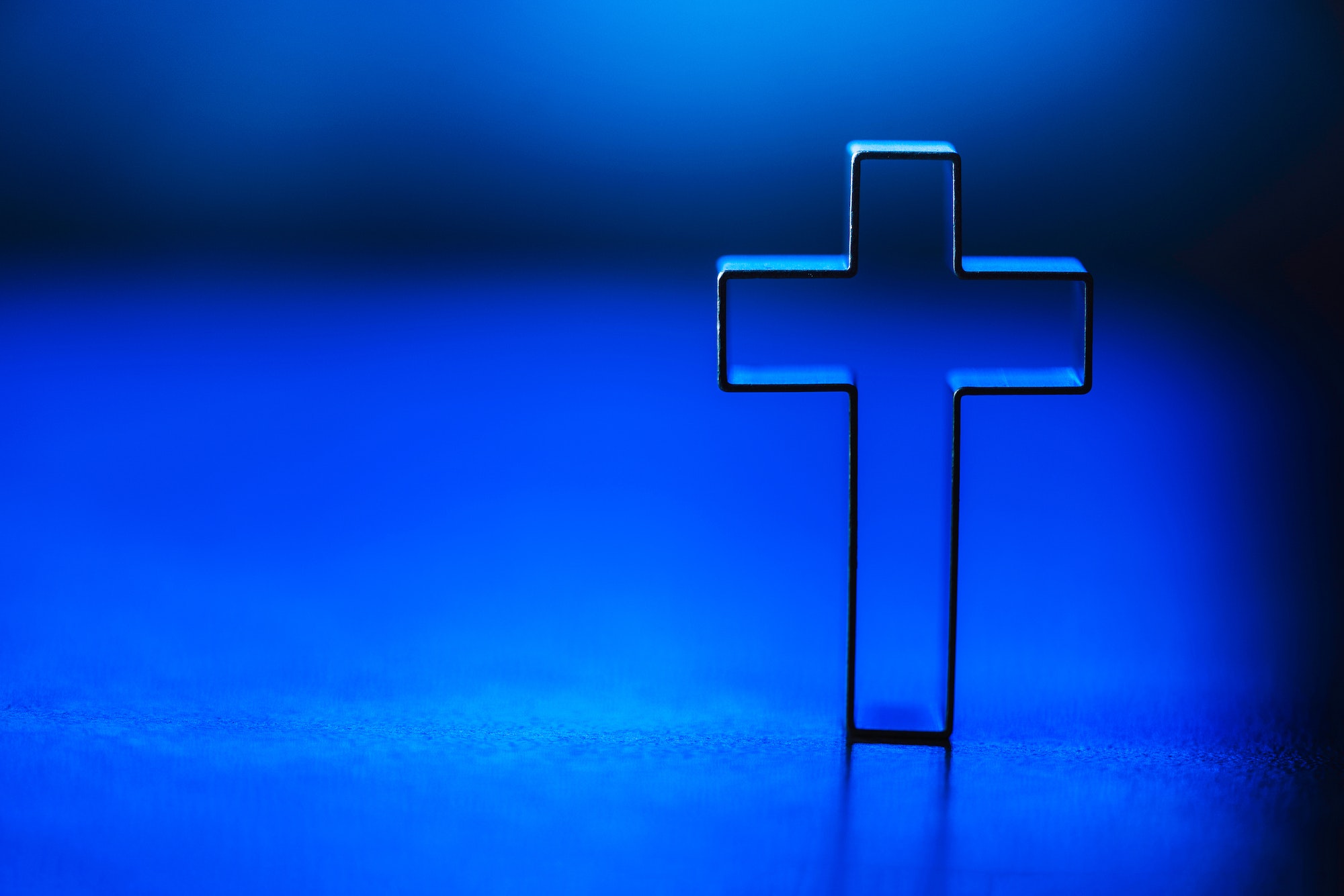 Silhouette of christian cross on blue background, soft bokeh lights background. Copy space. Church